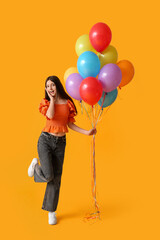 Surprised teenage girl with colorful air balloons on yellow background