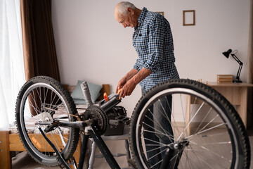 Caucasian retired man repairs bicycle at home. Attentive elderly man opens toolbox. Leisure and DIY.