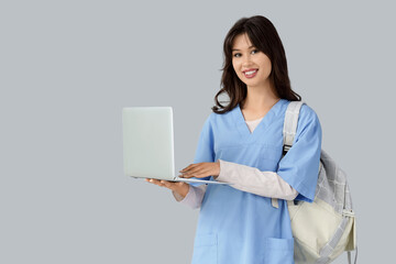 Female medical intern with backpack using laptop on light background