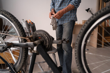 An elderly man repairs a bicycle in an apartment. A Caucasian man independently maintains his...