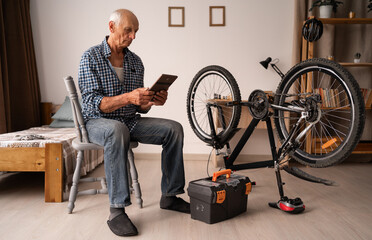An elderly Caucasian pensioner is enthusiastically repairing his bicycle at home. The man is...