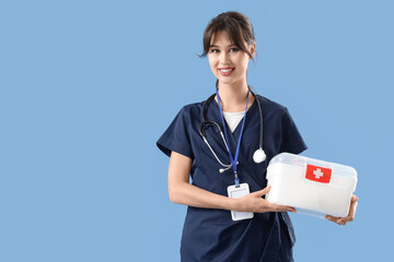 Female medical intern with first aid kit on blue background