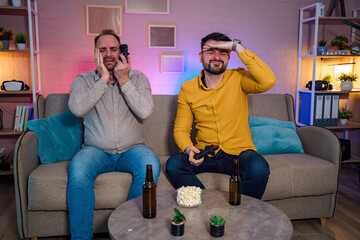 Two friends enjoying a gaming night with snacks and drinks indoors