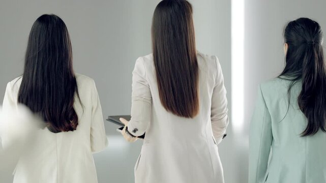 Three women are walking down a hallway. One of them is wearing a white jacket. The other two are wearing green jackets