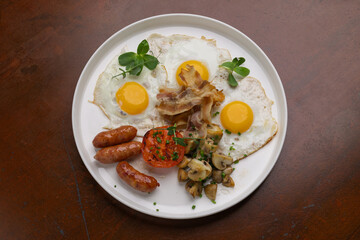 Sizzling breakfast plate features sunny-side-up eggs, savory sausages, grilled tomatoes, and sauteed mushrooms. Perfect morning meal.