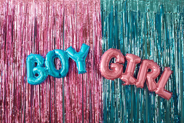 Blue balloon letters spelling boy and pink balloon letters spelling girl hanging against metallic...