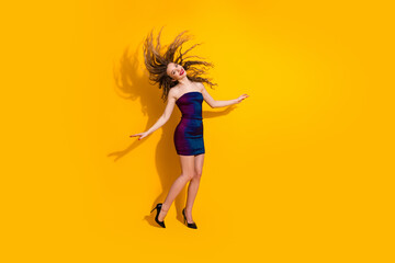 Beautiful young woman dancing in vibrant dress on yellow background showcasing energy, fashion, and festive celebration vibes