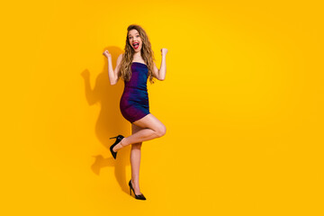 Fashionable young woman in a shimmering dress celebrating against a vibrant yellow backdrop, radiating joy and charm