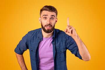 Great idea. Young Caucasian guy pointing finger upwards, gesturing eureka, having inspirational AHA moment on orange studio background. Millennial man finding solution to complicated problem