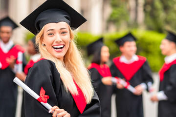 Happy young woman student cheerfully posing while graduation party, wearing graduation robe and...