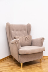 Beige armchair with tufted backrest placed in a minimalist room corner. The soft fabric and wooden legs create a cozy and inviting atmosphere on the polished wooden floor