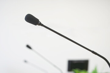 Row of black gooseneck microphones aligned on a wooden table against a white wall with a blurred monitor. Ideal for illustrating business meetings, press conferences, or audio setups. Photo