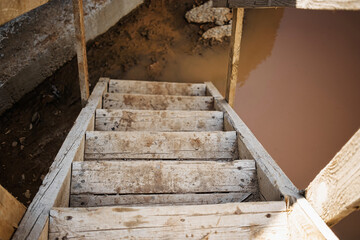 Wooden stairs leading down to murky water near a construction site during daylight hours