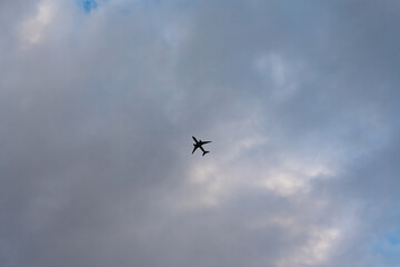 Dark silhouette of a passenger airplane flying high in the sky against a background of dense,...