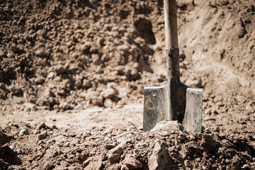 Shovel resting on freshly dug earth at a construction site under clear skies during daylight