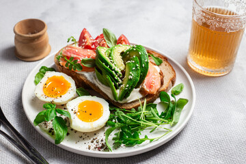  Sandwich with salmon, avocado, tomatoes and egg in a white plate on the table close-up. Healthy breakfast