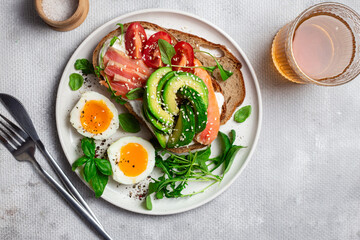  Sandwich with salmon, avocado, tomatoes and egg in a white plate on the table close-up. Healthy breakfast