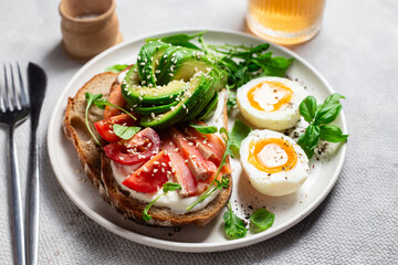  Sandwich with salmon, avocado, tomatoes and egg in a white plate on the table close-up. Healthy breakfast
