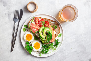 Sandwich with salmon, avocado, tomatoes and egg in a white plate on the table close-up. Healthy breakfast