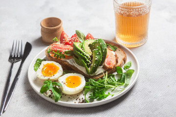  Sandwich with salmon, avocado, tomatoes and egg in a white plate on the table close-up. Healthy breakfast