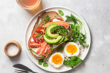  Sandwich with salmon, avocado, tomatoes and egg in a white plate on the table close-up. Healthy breakfast