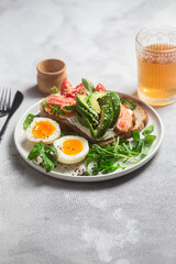  Sandwich with salmon, avocado, tomatoes and egg in a white plate on the table close-up. Healthy breakfast