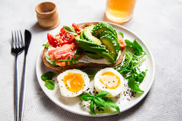  Sandwich with salmon, avocado, tomatoes and egg in a white plate on the table close-up. Healthy breakfast