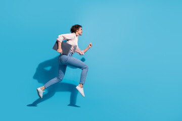 Young businesswoman in pink satin blouse running against blue background with laptop in hand,...