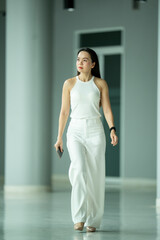 A woman wearing a white dress and white pants walks down a hallway