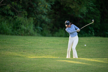 A woman is swinging a golf club on a grassy field