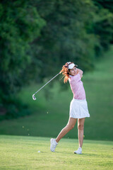 A woman is swinging a golf club on a green field