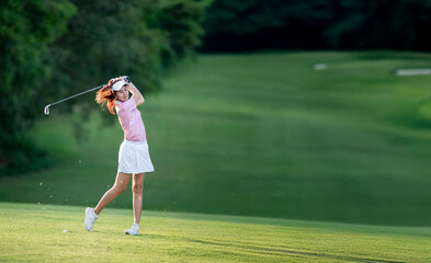 A woman in a pink shirt and white skirt is swinging a golf club