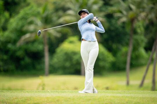 A woman is swinging a golf club on a golf course