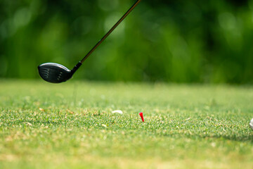 A golf club is in the air and a red golf ball is on the ground