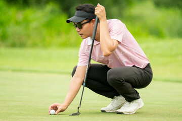 A man in a pink shirt is bending over to pick up a golf ball