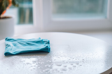 Folded blue microfiber cloth lying on a freshly cleaned white tabletop with water droplets. High quality photo