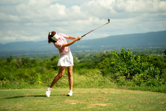 A woman is swinging a golf club on a golf course