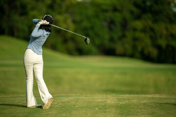 A woman is swinging a golf club on a grassy field