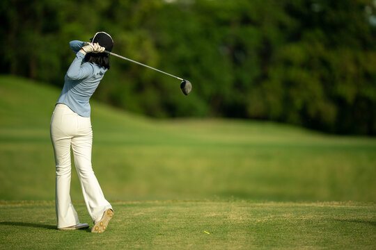 A woman is swinging a golf club on a grassy field