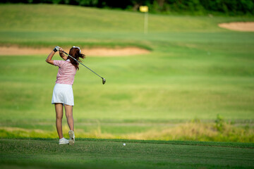 A woman is playing golf and swinging her club