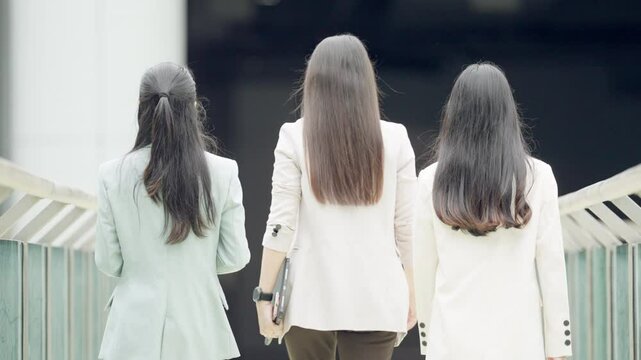 Three women are walking down a bridge. One of them is wearing a white jacket. The other two are wearing green jackets