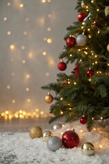 Fototapeta premium Closeup of decorated christmas tree with red and gold ornaments and fairy lights on snowy ground
