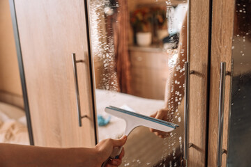 Cleaning a wardrobe mirror with a rubber squeegee, removing soap and water during routine household chores. High quality photo