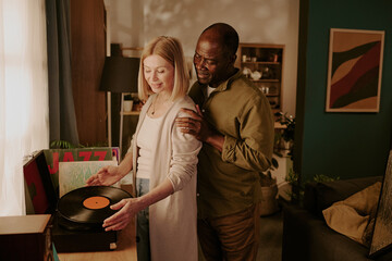 Senior Caucasian woman and senior Black man standing together, smiling and listening to vinyl...
