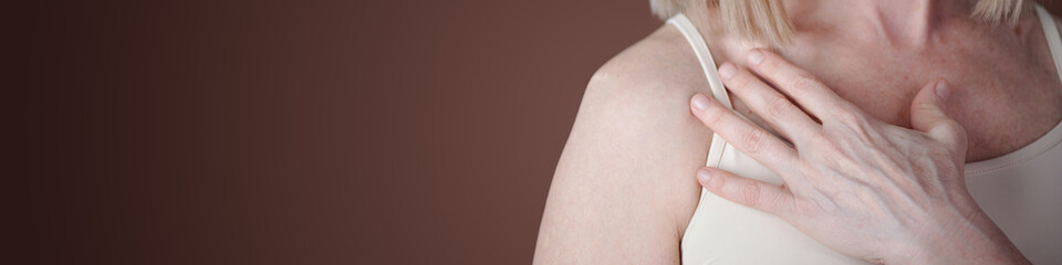 Image showing woman touching her shoulder with hand, partly visible in soft lighting. Image emphasizes gentle and soft touch with focus on skin texture