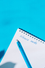 Notebook with handwritten silence mode and a blue pen on turquoise blue background. Creative flat lay for digital detox or focus mode themes. High quality photo