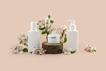 cosmetics containers on a wooden podium and branches of a blooming apple tree on a beige background