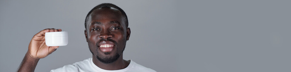 African American man smiling and holding white container against plain background. Copy space available on right side of image