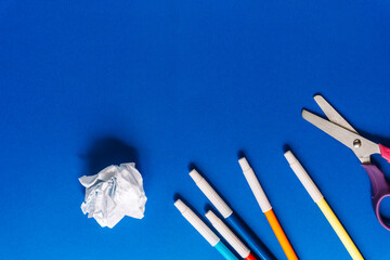 Top view of colorful markers, a crumpled paper ball and scissors arranged on a vivid blue background. School or office supplies creative layout. High quality photo