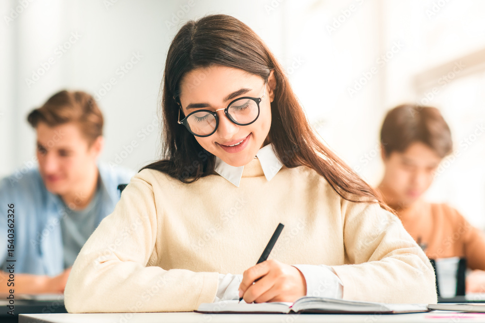 Poster studying and learning concept. portrait of smiling young woman in eyeglasses sitting at table in lec
